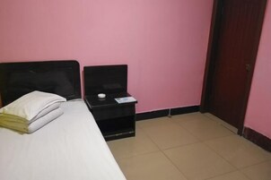 Una habitación pequeña con una cama, una mesita de noche, una puerta y una pared rosa.