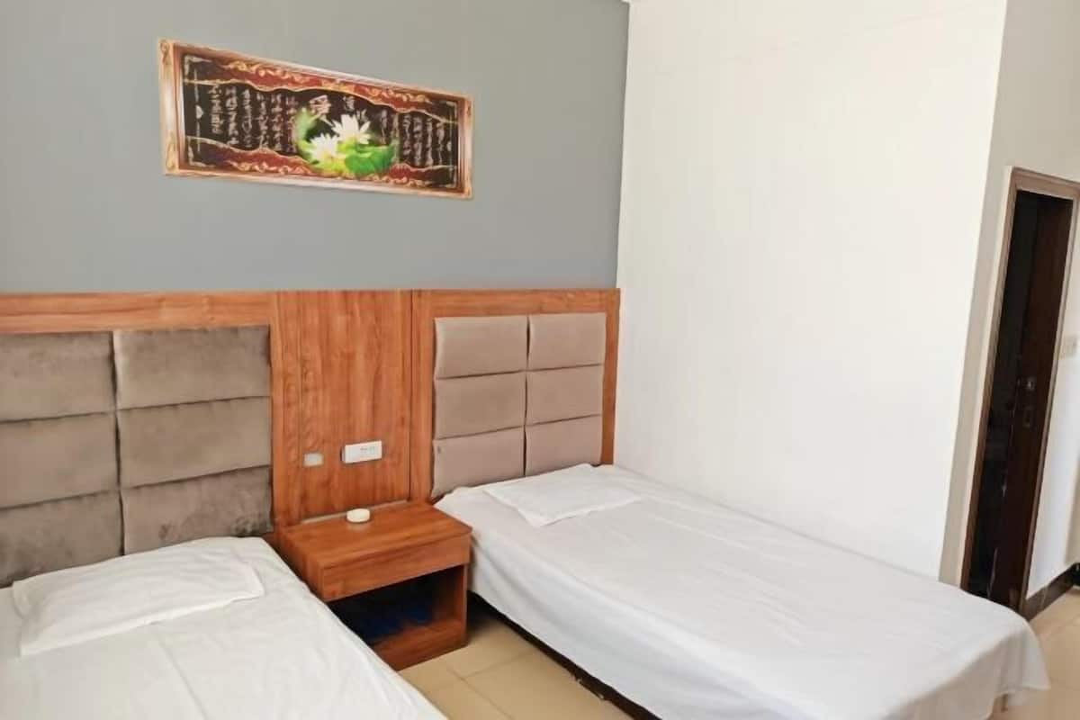 Ein Schlafzimmer mit zwei Einzelbetten, einem Holzkopfende, einem Nachttisch und einem an der Wand hängenden Kunstwerk.