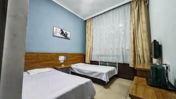 A hotel room with two beds, a wooden headboard, a small table, a TV, and a window with curtains.