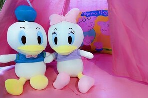 Two plush toys, one with a blue hat and the other with a pink bow, sitting on a pink surface with a colorful background.