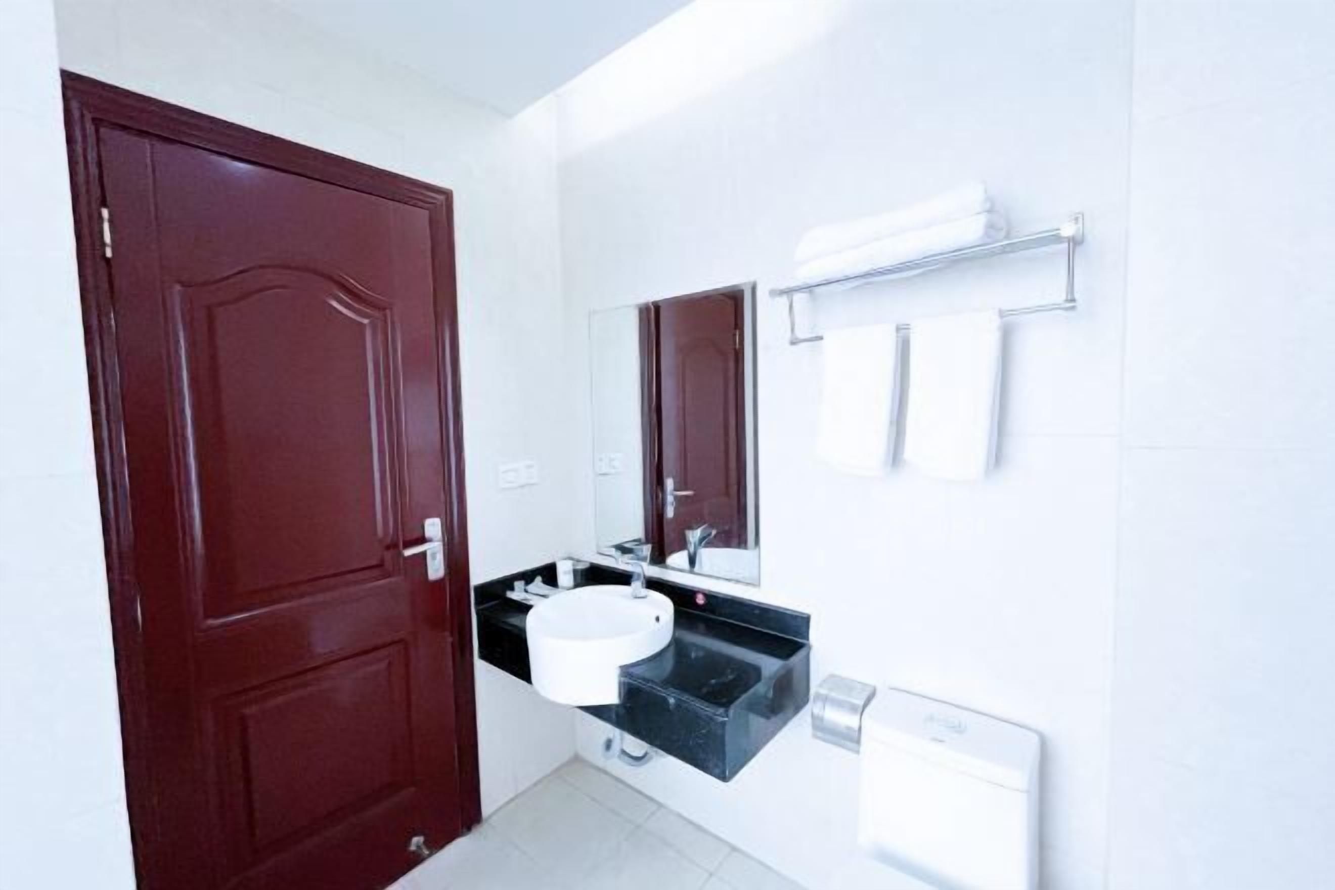 Une salle de bain avec une porte rouge, un lavabo noir, des toilettes blanches et un miroir au-dessus du lavabo.