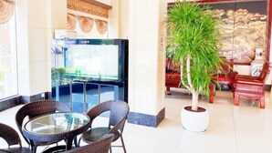 Un hall d’entrée avec des fauteuils en osier disposés autour d’une table en verre, une grande plante en pot et un téléviseur posé sur un meuble.