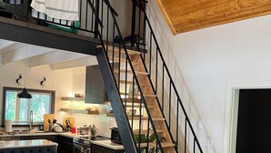 A modern kitchen with a central island, a dining area with a bench, and a staircase leading to an upper level. - Little Giant, concrete built
Serene 2-bedroom house with WiFi in charming Coram  (Coram)