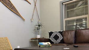 A modern living room with a wooden coffee table, a brown leather sofa, a woven chair, and a potted plant. - Little Giant, concrete built
Serene 2-bedroom house with WiFi in charming Coram  (Coram)