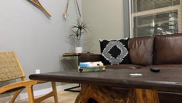 Uma sala de estar moderna com uma mesa de centro de madeira, um sofá de couro marrom, uma cadeira de fibra natural e um vaso com planta.