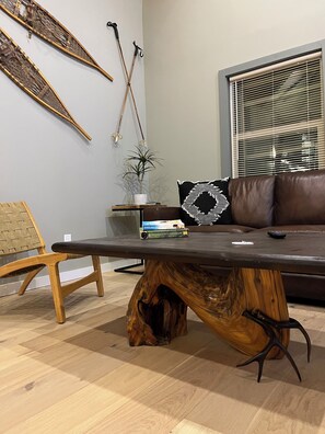 Un salon moderne avec une table basse en bois, un canapé en cuir marron, un fauteuil en osier et une plante en pot.