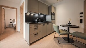 A modern kitchen with built-in appliances, a dining area with a round table and two chairs, and a hallway leading to another room. - Gipfelglück Standard (Kirchberg in Tirol)