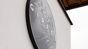 A circular sign with the text "GIPFEL" and a signature on a building facade. - Gipfelglück Standard (Kirchberg in Tirol)