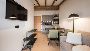 A modern kitchen with built-in appliances, a dining area with a table and chairs, and a living area with a sofa and a TV. - Gipfelglück Comfort light (Kirchberg in Tirol)