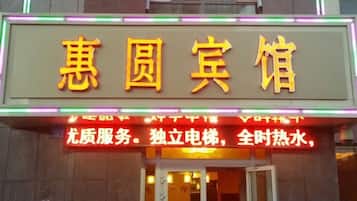A hotel sign with Chinese characters and a neon sign below stating services like 'high-quality service' and '24-hour hot water.'