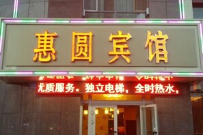 A hotel sign with Chinese characters and a neon sign below stating services like 'high-quality service' and '24-hour hot water.' - HUIYUAN HOTEL (Korla)