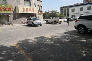 A parking area with vehicles, a building with signage, and a pedestrian walkway. - HUIYUAN HOTEL (Korla)