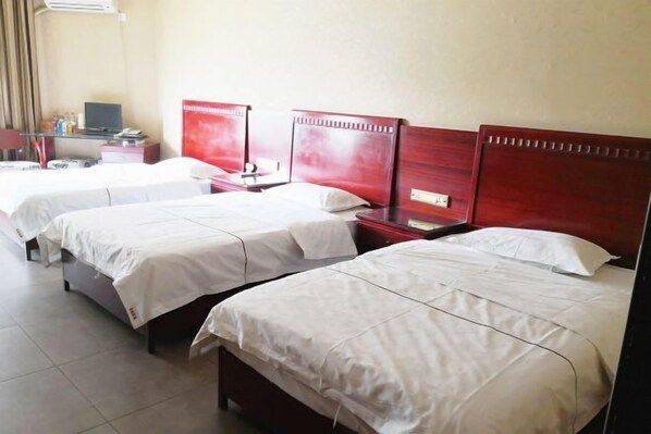 Habitación de hotel con tres camas individuales, un escritorio con computadora y televisión.