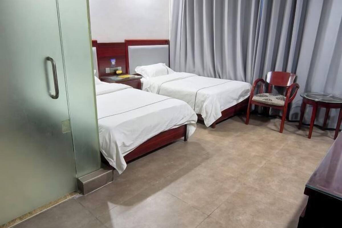 A hotel room with two beds, a chair, a small table, and a wardrobe.