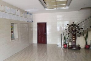 A spacious lobby with a polished floor, a red door, and a decorative ship's wheel. - HUIYUAN HOTEL (Korla)