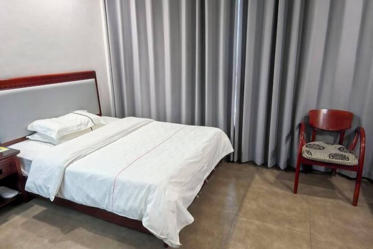 A hotel room with a bed, a chair, and a window with curtains.