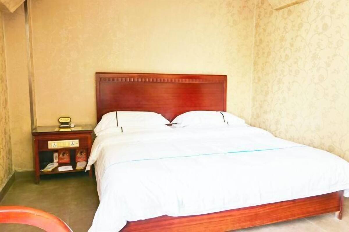 A neatly made bed with a wooden headboard, a small bedside table with a lamp, and a wall with a floral pattern.