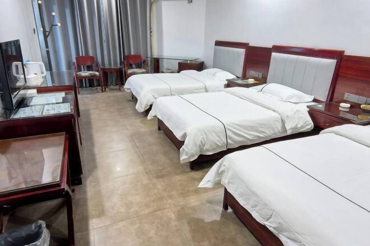 A hotel room with three beds, a desk with a computer, and a chair.