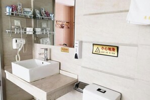 A bathroom with a white sink, a mirror, and a towel rack. There is a sign with Chinese characters and a warning symbol. - HUIYUAN HOTEL (Korla)