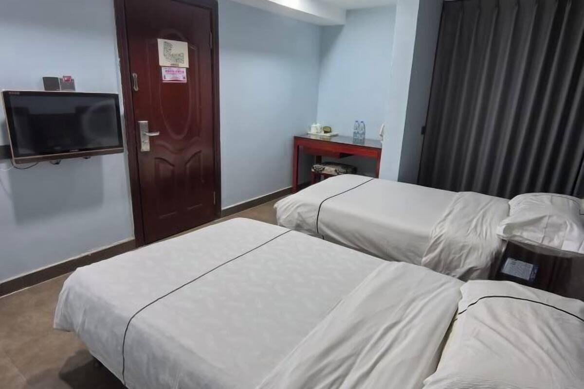 A hotel room with two beds, a TV, a desk with a chair, and a window with curtains.