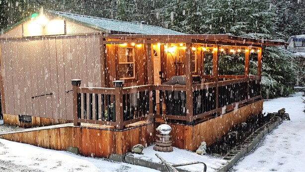 A wooden cabin with a porch and lights, surrounded by snow.