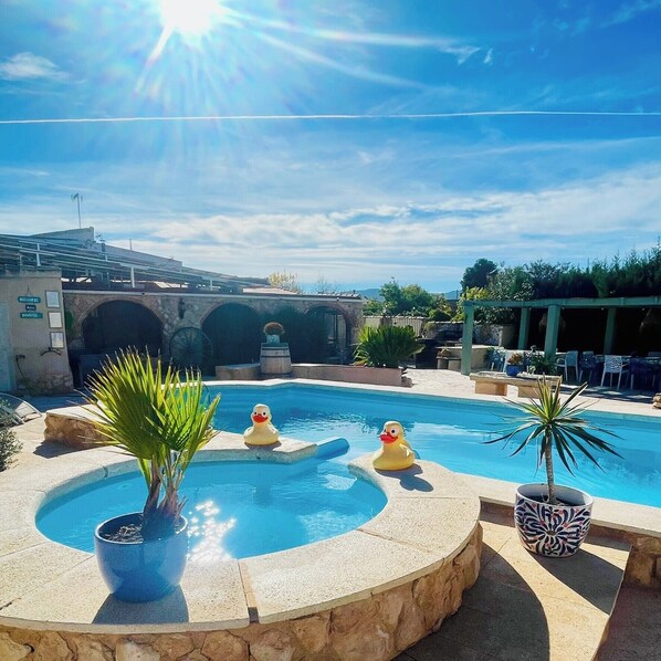 A swimming pool with two rubber ducks, a stone bridge, and a clear sky.