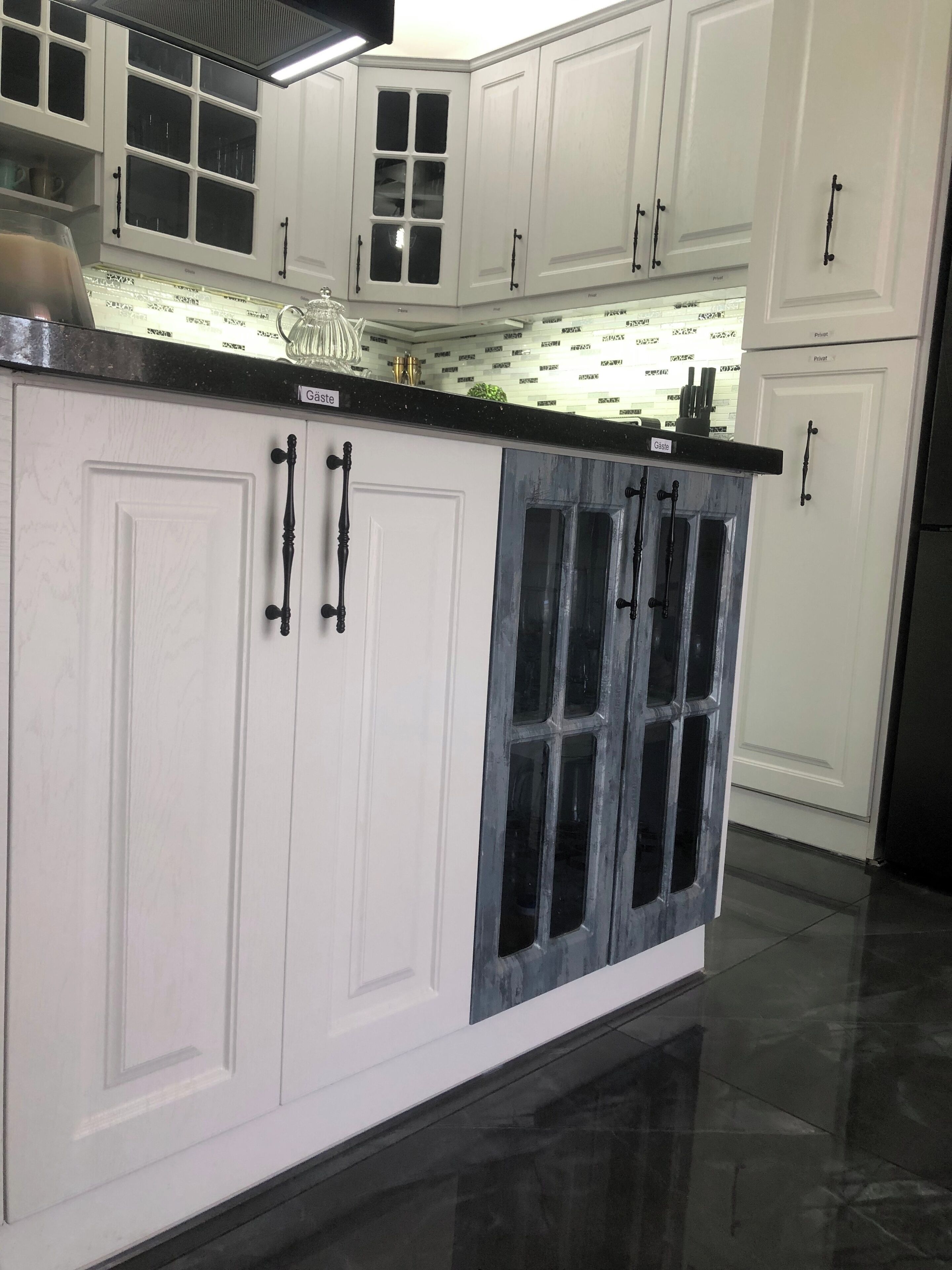 A modern kitchen with white cabinetry, a black countertop, and a glass-enclosed island.