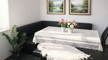 A room with a black leather bench, a white table with a lace table runner, two framed landscape paintings, and a potted plant.