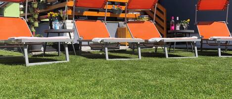 Een terras met oranje lounge stoelen, een houten pergola en potplanten.