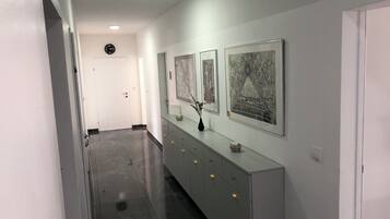 Ein Flur mit einem langen, schmalen, hellen Schranksystem an der Wand, das von zwei gerahmten Kunstwerken eingerahmt wird.