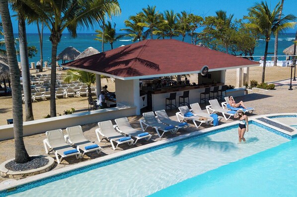Un espace aménagé au bord de la piscine, avec des chaises longues, un bar et une vue sur l’océan.