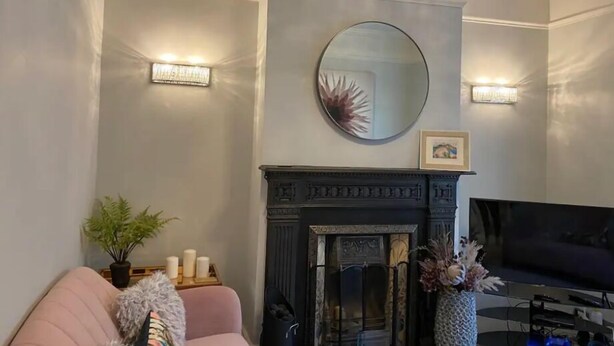 A living room with a fireplace, a round mirror, and a television. - Luxury Central Hale  living (Altrincham)