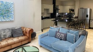 A modern living room with a brown leather sofa and a blue sofa with a pillow stating "New York Paris Hale". - Luxury Central Hale  living (Altrincham)