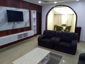 Un salon moderne doté d’un grand téléviseur à écran plat fixé sur un mur en marbre, d’un canapé en cuir noir et d’une petite table basse blanche.