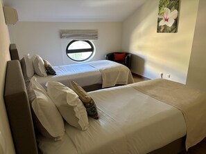 Ein Zimmer mit zwei Betten, einem Fenster, einem Sessel und einer Wand-Klimaanlage.