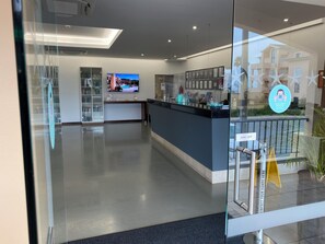 Ein moderner Empfangsbereich mit Glastrennwand, einer Rezeption, einem Wandfernseher und einer Vitrine mit Zertifikaten.