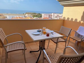 Ein Balkon mit Frühstückstisch, Stühlen und Blick auf das Meer und die Gebäude.
