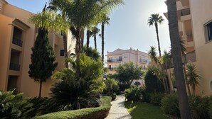 Une cour avec un chemin pavé, des palmiers et un bâtiment doté de balcons.