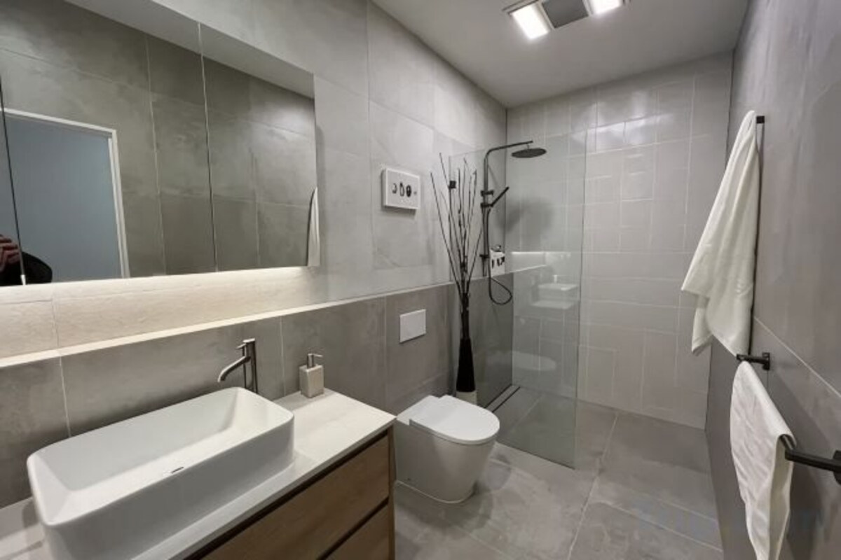 A modern bathroom with a large mirror, a sink, a toilet, and a glass-enclosed shower area.