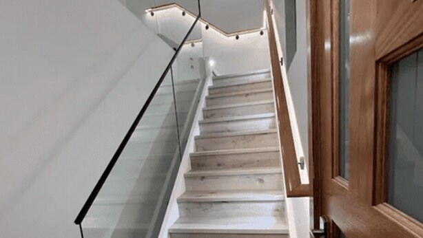 Una escalera con escalones de madera y barandilla de vidrio, que lleva a una puerta con marco de madera.