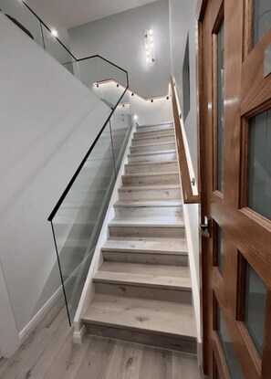 Una escalera con escalones de madera y barandilla de vidrio, que lleva a una puerta con marco de madera.