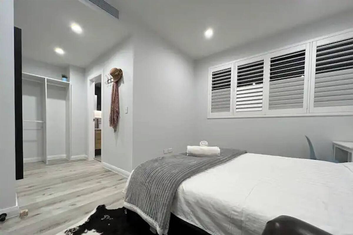 A modern bedroom with a bed, a small desk, a chair, and a wardrobe.