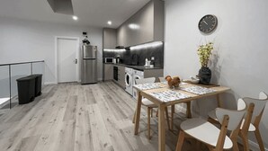Una cocina moderna con electrodomésticos de acero inoxidable, una zona de comedor con mesa y sillas, y un reloj en la pared.