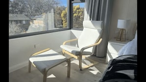 Una habitación moderna con un ventanal grande, un sillón blanco, una mesita y una lámpara de noche.