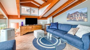 Una sala moderna con un sofá azul, vigas de madera, un televisor y una ventana.