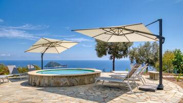 Una piscina in pietra con due ombrelloni, lettini e vista sul mare.