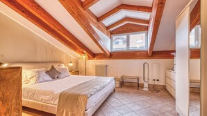 Un dormitorio con una cama grande, vigas de madera, un radiador, un banco y un aparador.