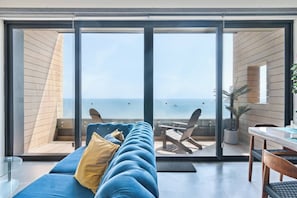 A modern room with a blue sofa, a dining table, and a view of the sea through large glass doors.