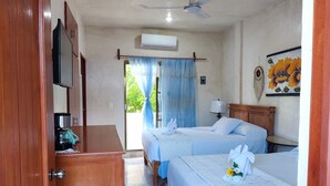 Egy szállodai szoba két ággyal, mennyezeti ventilátorral, légkondicionálóval, kávéfőzővel és egy falfestménnyel.