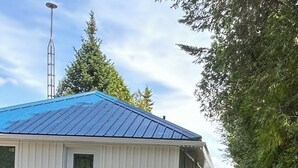 Eine kleine, eingeschossige Holzhütte mit blauem Dach, einer Eingangstür und einer Veranda mit blauen Stühlen.